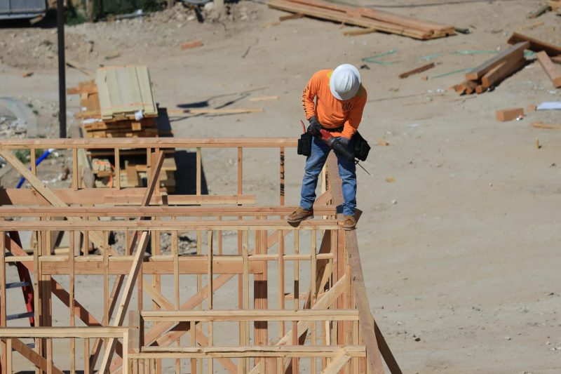 A construction worker in a safety helmet drills into a wooden framework at a construction site.