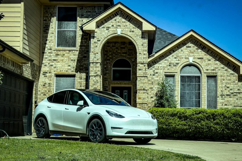 Stylish white electric car parked by a classic brick house under bright sunlight.