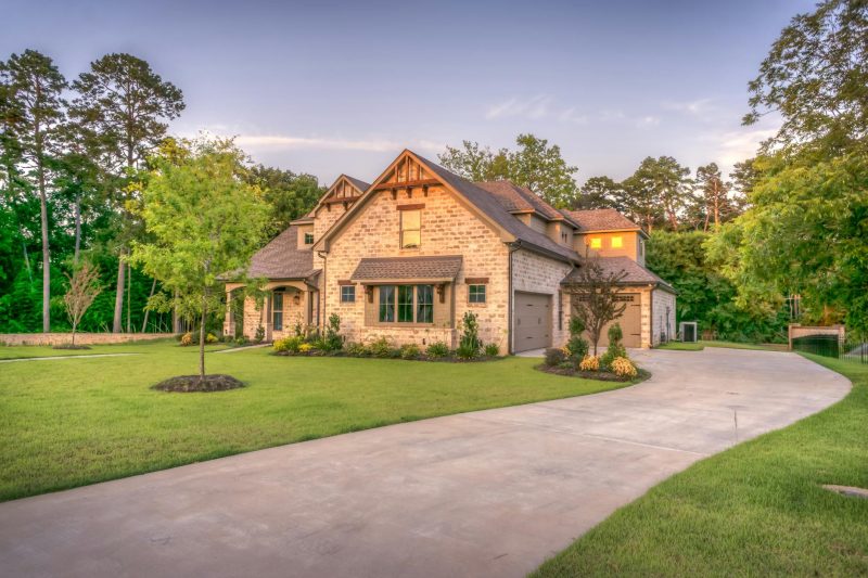 Elegant stone family home with a lush lawn, surrounded by trees and a vibrant garden.
