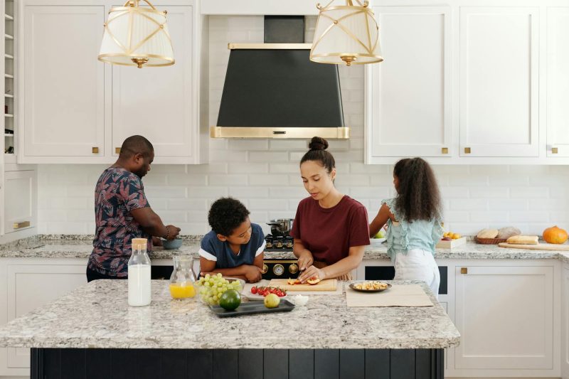 A family cooks together in a bright, modern kitchen, surrounded by fresh ingredients and smiling faces.