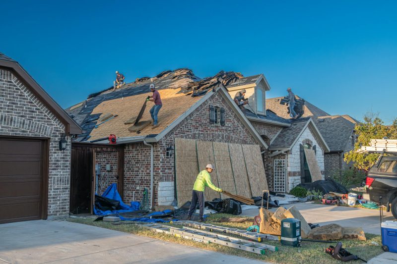 Workers replace the roof of a brick house in Fort Worth, Texas on a sunny day.