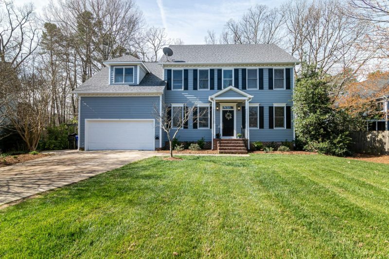 Bright suburban family home with a spacious lawn and classic architecture, surrounded by greenery.