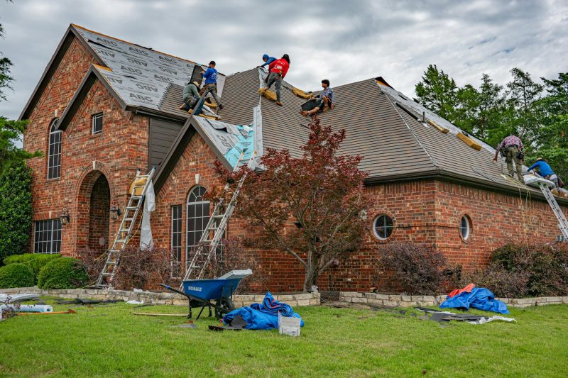 Roofers applying shingles on a brick home under a clear sky in Allen, Texas.