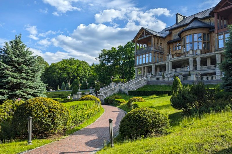 Stunning wooden manor surrounded by manicured gardens and vibrant trees under a clear blue sky.