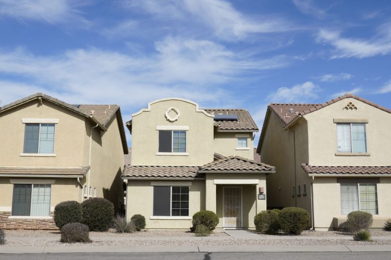 Three adjacent houses in a Tucson suburban neighborhood under a clear blue sky.