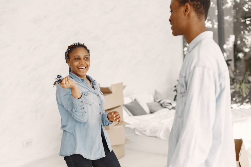 Smiling couple indoors holding house keys, celebrating their new home together.
