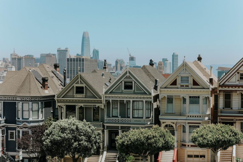 Colorful Victorian houses in San Francisco with a city skyline backdrop under a clear blue sky.