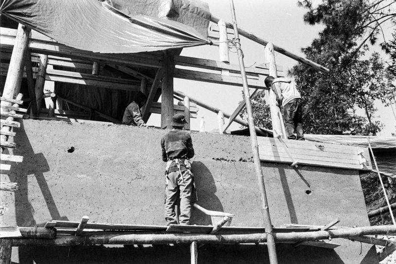 Workers in hard hats operate on a construction site, surrounded by scaffolding and building materials.