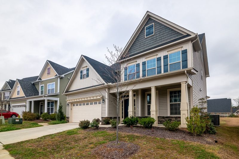 Row of modern suburban homes with garages, driveways, and well-maintained lawns under clear daylight.