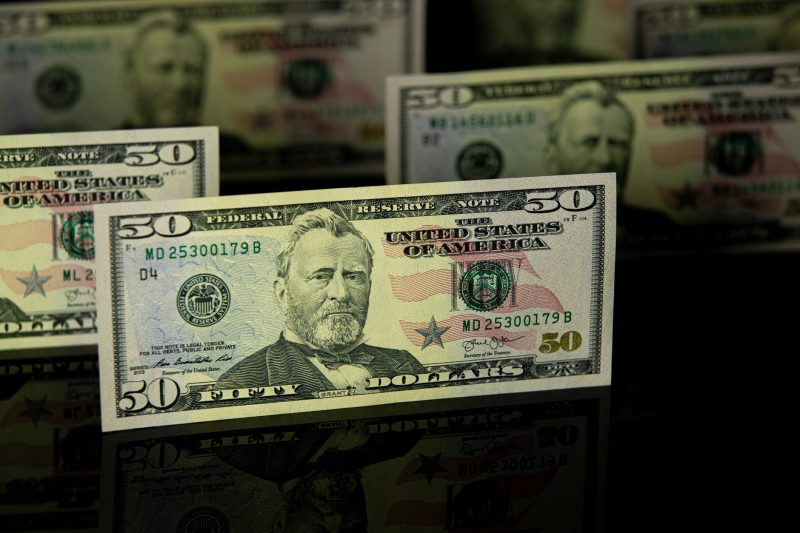 Fifty dollar bills arranged on a dark reflective surface, emphasizing a sense of wealth.