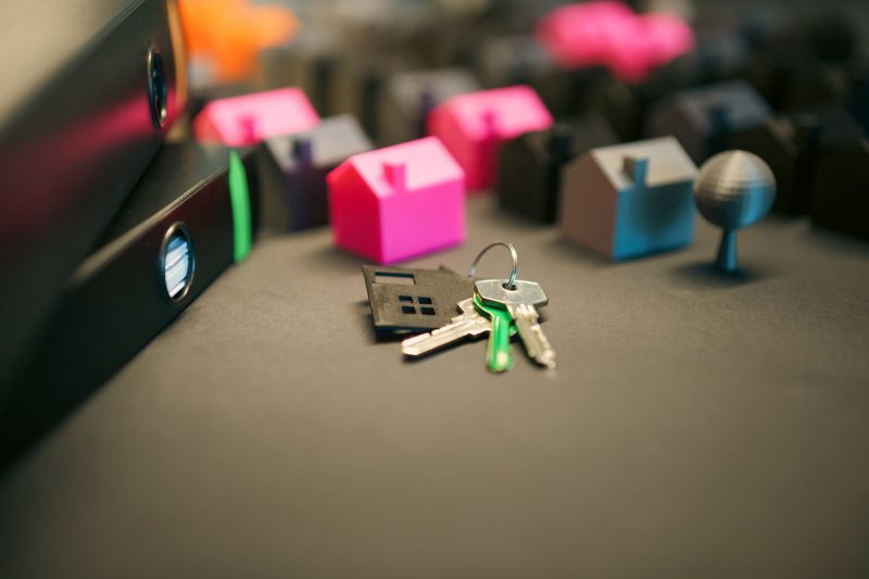 Miniature model houses and a set of keys on a wooden desk.